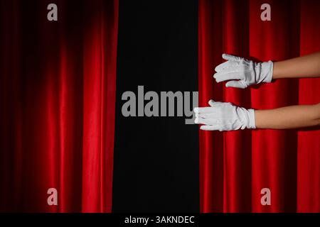 Mani femminili in guanti con tende rosse su sfondo nero Foto Stock