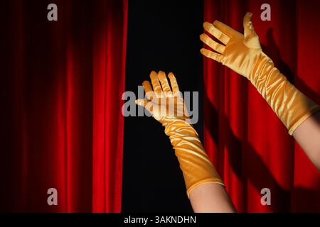 Mani femminili in guanti e tende rosse aperte su sfondo nero Foto Stock