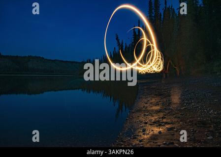 Il fuoco gira la vista, lo sfondo, la carta da parati lungo il lato di un lago con foresta, boschi, cielo scuro, riflessi. Preso sul fiume Teslin, territorio dello Yukon Foto Stock