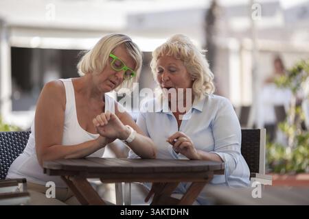 Due donne di mezza età chiacchierano in un bar, controllando l'orologio Foto Stock