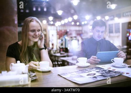 Donna sul suo cellulare di bere il caffè accanto all uomo in possesso di una smart tablet Foto Stock