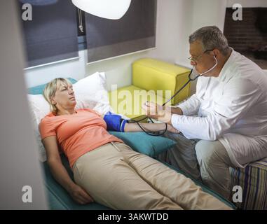 Senior donna è sotto controllo medico a casa. L'uomo controllare la pressione sanguigna con tonometro e stetoscopio Foto Stock