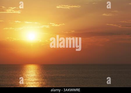 Spettacolare tramonto tropicale arancione su un oceano calmo con un fascio di luce riflesso sull'acqua calma Foto Stock
