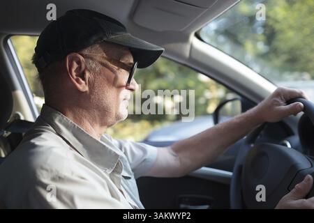 Vista laterale di un uomo anziano con gli occhiali alla guida di una vettura su una soleggiata giornata estiva Foto Stock