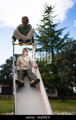 Due fratelli giocano su uno scivolo in un parco giochi durante una giornata estiva Foto Stock