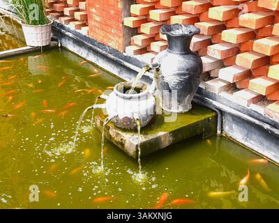 vista dall'alto di una fontana decorativa in uno stagno di pesci mossy e non spietato Foto Stock