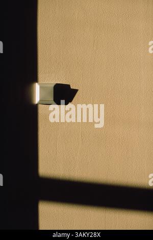 Minimalismo geometrico con una parete beige, un'ombra quadrata e un piccolo interruttore luminoso Foto Stock