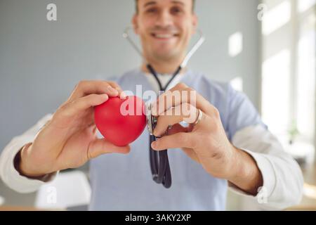Medico di sesso maschile cardiologo con stetoscopio che esamina il cuore rosso in piedi in clinica medica. Foto Stock