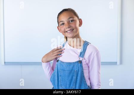 Ragazza sorridente in classe con tute in denim e camicia rosa Foto Stock