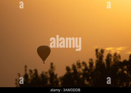 Una mongolfiera galleggia con grazia nel bagliore arancione del tramonto, che si staglia contro il radioso cielo dorato. Foto Stock