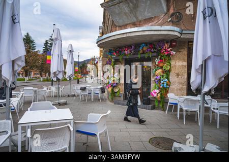 Deva, Romania - 11 aprile 2025 una donna cammina davanti a un caffè il cui ingresso ha mazzi di fiori artificiali piante e cesti di vimini. Foto Stock