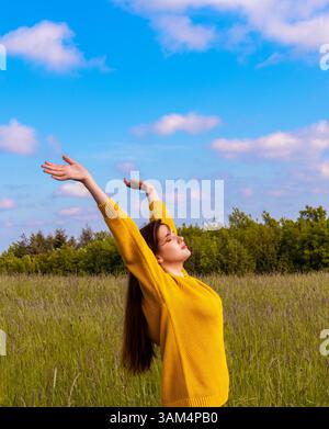 La bella giovane donna con le braccia alzate gode dell'ora primaverile al mattino Foto Stock