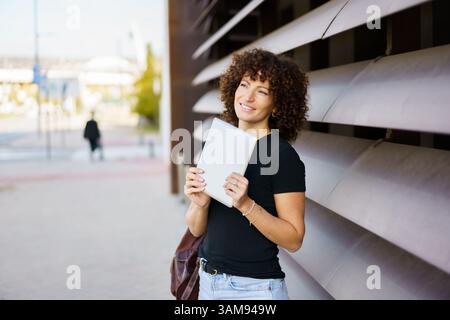 Una giovane donna sicura di sé che tiene in mano un tablet all'aperto in un ambiente urbano moderno Foto Stock