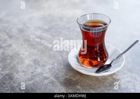 Tradizionale chai turco in un vetro a forma di tulipano siede su un piattino con un cucchiaio su un tavolo di marmo e spazio per le copie Foto Stock