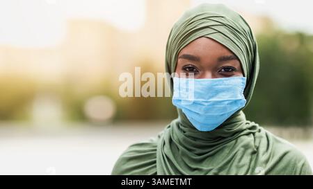 Donna musulmana africana felice in hijab indossando maschera facciale protettiva all'aperto Foto Stock