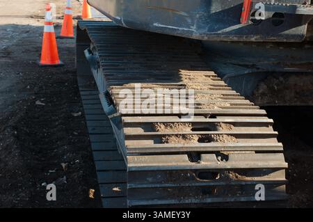 Attrezzature per l'edilizia pesante in un cantiere con coni per il traffico. Primo piano di macchinari cingolati per impieghi gravosi in un cantiere, con coni stradali inseriti Foto Stock