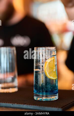 Cocktail blu con limone e ghiaccio in un bicchiere sul tavolo. Foto Stock