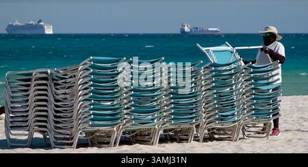 L'uomo mette i lettini sulla spiaggia con le navi all'orizzonte Foto Stock