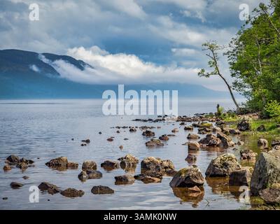 Il sole sulla riva orientale del Loch Ness nelle Highlands scozzesi, mentre le nuvole si infrangono sulle colline sulla riva occidentale. Foto Stock