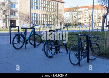 Poznan, Polonia - 8 aprile 2025: Vari tipi di biciclette saldamente bloccate su scaffali in metallo nero su un marciapiede della città vicino a edifici residenziali, re Foto Stock