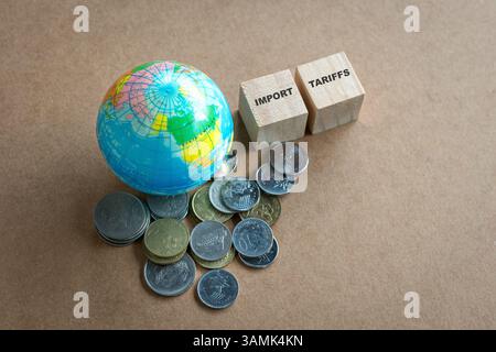 Tariffe d'importazione, messaggio in cima a blocchi di legno quadrati e accanto a globo e monete in miniatura. Foto Stock