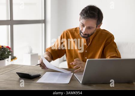 Uomo d'affari maturo e concentrato che lavora in un ufficio domestico e si occupa di contabilità Foto Stock