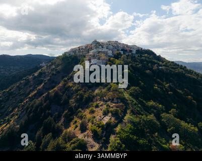 Vista aerea di un pittoresco villaggio collinare circondato da vegetazione lussureggiante e antichi edifici in pietra, Rotondella, Matera, Italia. Foto Stock