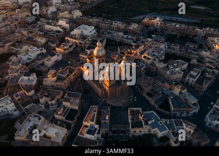 Veduta aerea della rotonda della chiesa di san giovanni battista circondata da edifici storici e pittoreschi tetti al tramonto, Dingli, Malta. Foto Stock