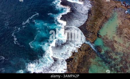 Vista aerea delle onde oceaniche che colpiscono la barriera corallina. Spettacolare vista aerea dall'alto verso il basso delle onde turchesi dell'oceano che si infrangono contro un'aspra barriera corallina e rocciosa Foto Stock