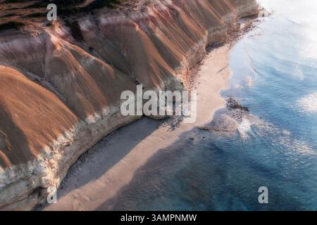 Vista aerea di una coppia che cammina su una spiaggia con scogliere calcaree che torreggiano sopra di loro e acqua blu dell'oceano che lambisce la costa, Port Willunga, Australia meridionale, Australia. Foto Stock