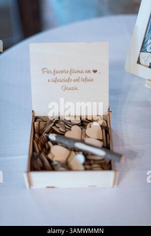 Una scatola di legno piena di gettoni a forma di cuore invita gli ospiti a firmare e lasciare messaggi al tavolo di un ricevimento di nozze. Foto Stock