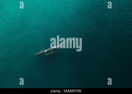 Vista aerea dall'alto verso il basso delle persone che pagaiano Su Una canoa rossa attraverso l'acqua dell'oceano turchese a Rio De Janeiro, Brasile. Foto Stock