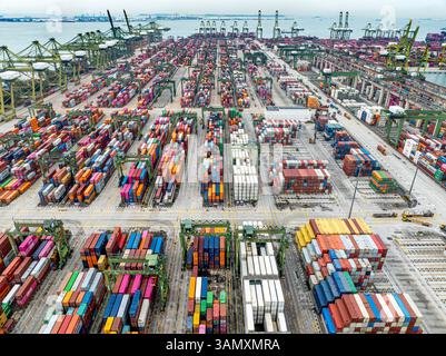 Singapore - 27 dicembre 2024: Veduta aerea dei colorati container impilati presso il terminal container del porto di Pasir Panjang con gru e molo Queen Foto Stock