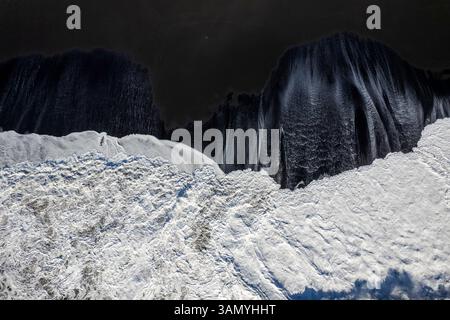 Veduta aerea dall'alto verso il basso della spiaggia di Reynisfjara, una spiaggia di sabbia nera lungo la costa dell'Islanda. Foto Stock