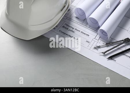Diversi disegni architettonici, elmetto, matita e divisore su tavolo grigio, primo piano. Spazio per il testo Foto Stock