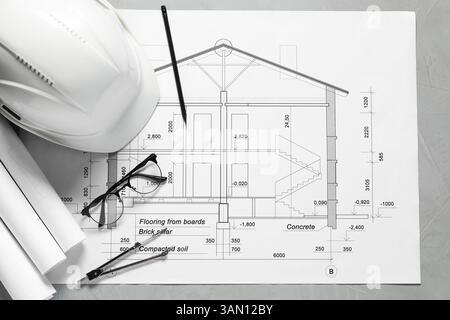 Diversi disegni architettonici, elmetto, matita, divisore e vetri su tavolo grigio, piatto Foto Stock