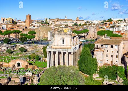 Rovine del foro Romano e del Tempio di Antonino e Faustina al centro, con il paesaggio urbano di Roma, Italia sullo sfondo. Foto Stock