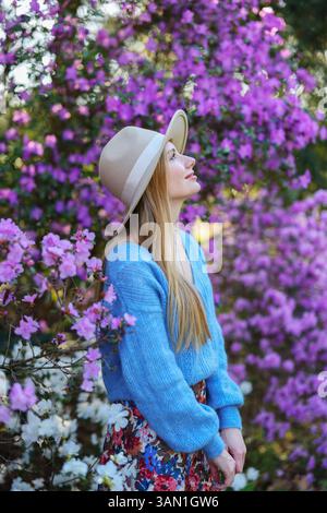 Momenti di pace all'aperto. Giovane donna con cappello e maglione blu in un paesaggio floreale Foto Stock