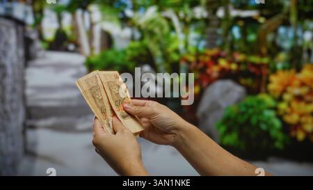 Uomo che detiene banconote brasiliane in un parco cittadino all'aperto, enfatizza il concetto di denaro, affari e transazioni finanziarie urbane. Foto Stock