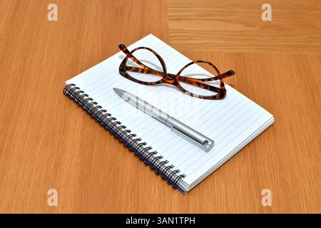 Penna, notebook e un paio di occhiali da lettura su un tavolo in ufficio Foto Stock