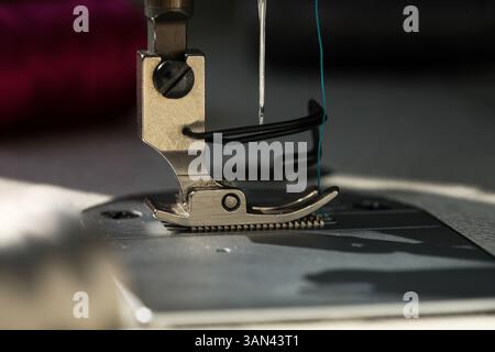 Un'immagine ravvicinata dell'ago e del piedino della macchina da cucire industriale con illuminazione naturale della giornata. Concetto creativo dei dettagli delle attrezzature da cucire Foto Stock