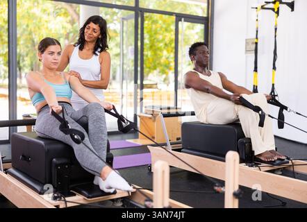 Istruttrice di pilates femminile ispanica che aiuta la giovane donna a fare esercizi sull'apparato riformatore Foto Stock