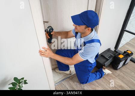 Lavoratore maschio con trapano elettrico che installa la piastra di battuta della porta a casa Foto Stock