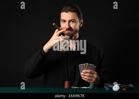 Bel giovane con whisky e sigaro che gioca a poker al tavolo del casinò Foto Stock