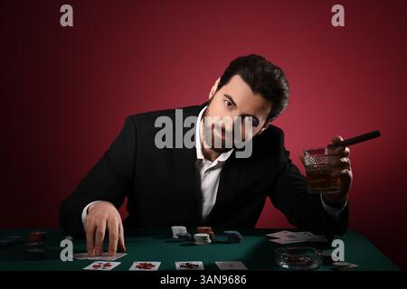 Bel giovane con whisky e sigaro che gioca a poker al tavolo del casinò Foto Stock