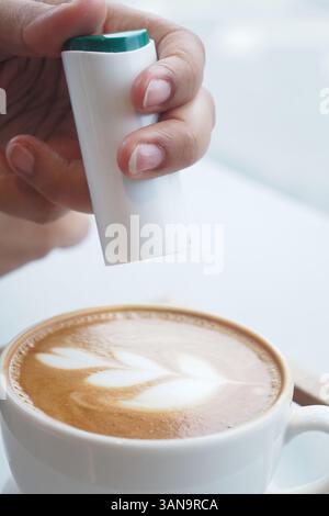 Primo piano di mani che spruzzano dolcificante nella tazza da caffè con latte Art Foto Stock