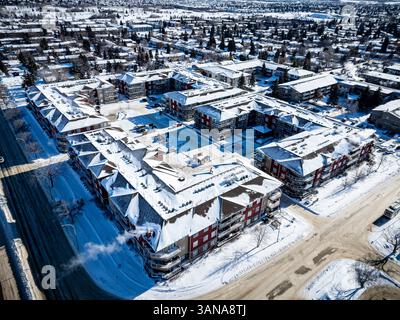 Paesaggio urbano innevato con un grande complesso di appartamenti nel centro. Gli edifici sono rossi e bianchi, e la neve copre il terreno. La scena ha un peacefu Foto Stock