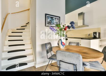 Interni eleganti e moderni con una scala ricurva graziosamente, un tavolo da pranzo rotondo, sedie contemporanee e un vivace centro floreale che migliora lo spazio. Foto Stock