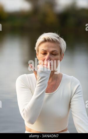Una donna adulta in tuta bianca è impegnata nello yoga kundalini, la pratica del Nadi-shodhana pranayama Foto Stock