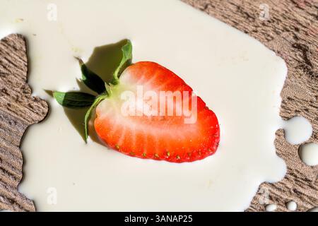 Mezza fragola (Fragaria x ananassa) in crema su legno rustico, simboleggia la freschezza, il piacere e la semplicità dei dessert estivi stagionali Foto Stock